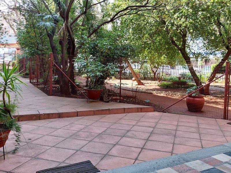 A paved outdoor patio area featuring tiled flooring, metal perimeter fencing, and established garden trees, providing a functional transition to the outdoor space.