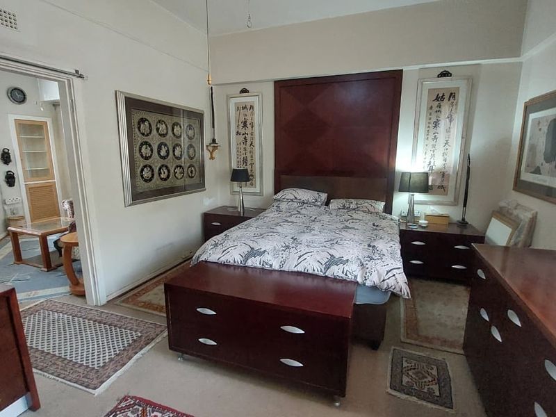 A spacious bedroom featuring a built-in headboard, picture rails, and coved ceilings, with an adjoining room visible through the doorway.