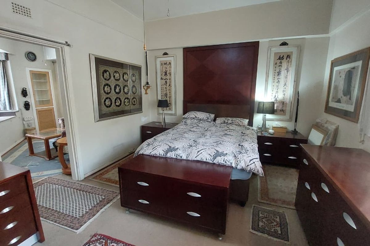 A spacious bedroom featuring a built-in headboard, picture rails, and coved ceilings, with an adjoining room visible through the doorway.