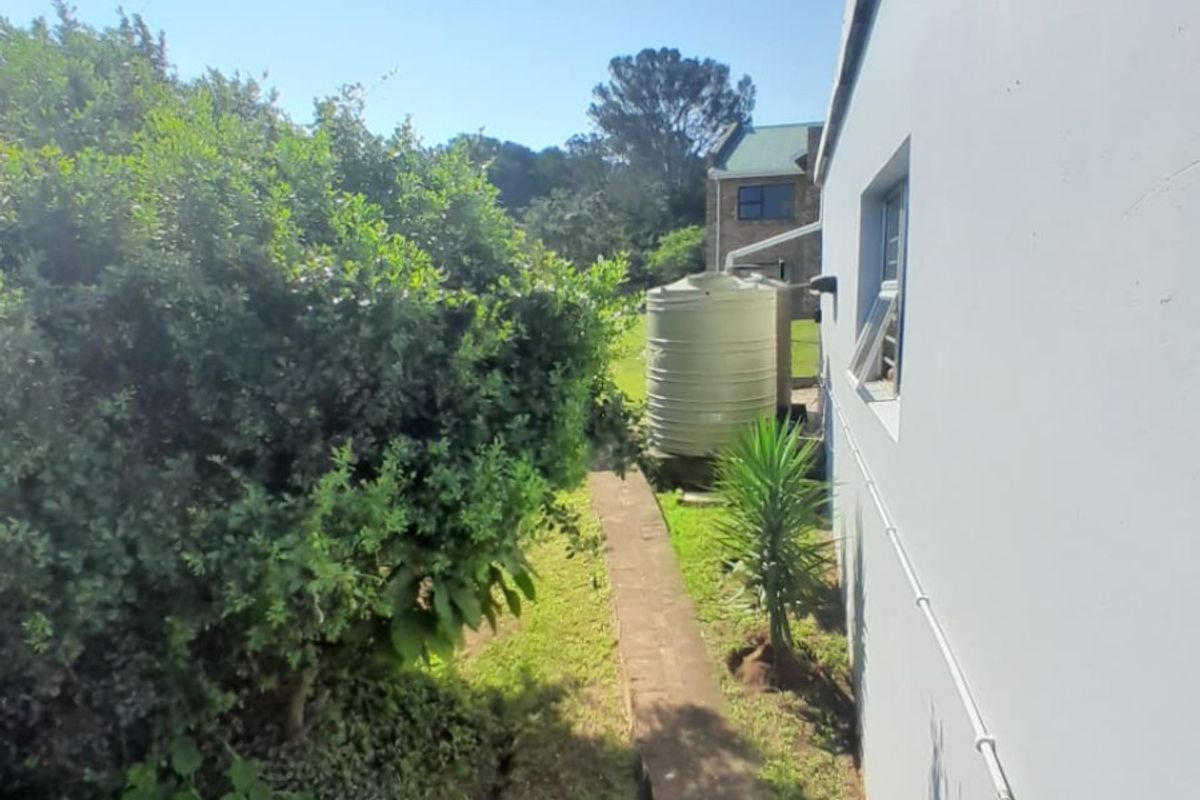 A view of the rear exterior side path featuring a water storage tank, paved walkway, and established garden greenery.