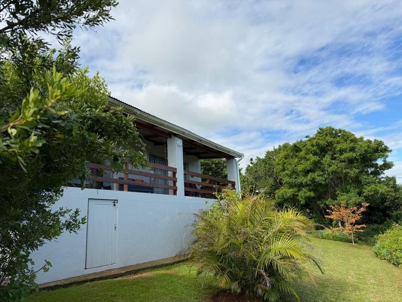 Rear view of the property featuring a covered patio with timber railing and a well-maintained garden area.