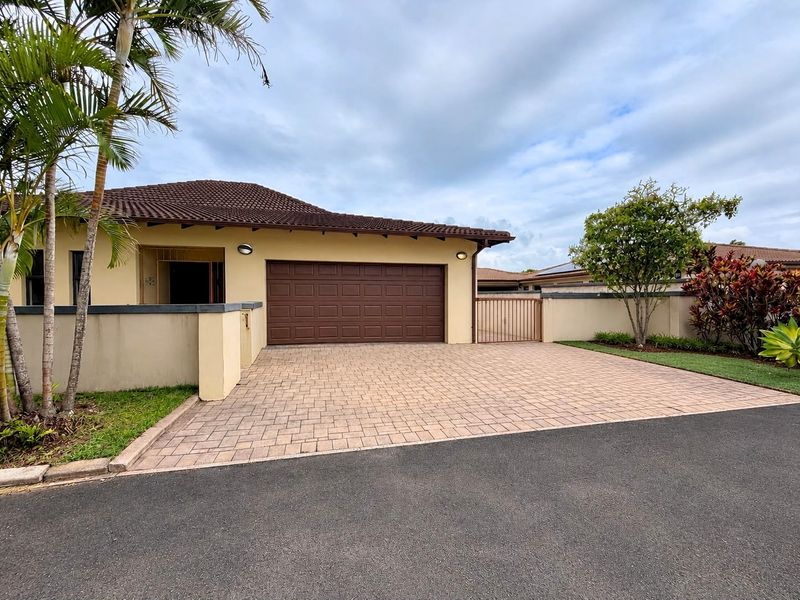 Front elevation of the property featuring a paved driveway, double garage, and secure boundary wall with pedestrian gate access.