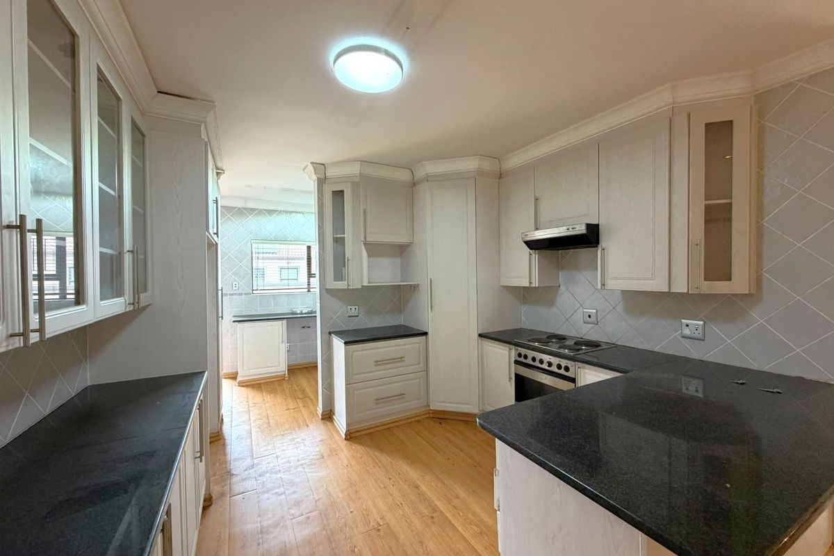 A spacious kitchen featuring light-toned built-in cabinetry, dark granite countertops, an electric hob, and an integrated oven with a tiled backsplash.