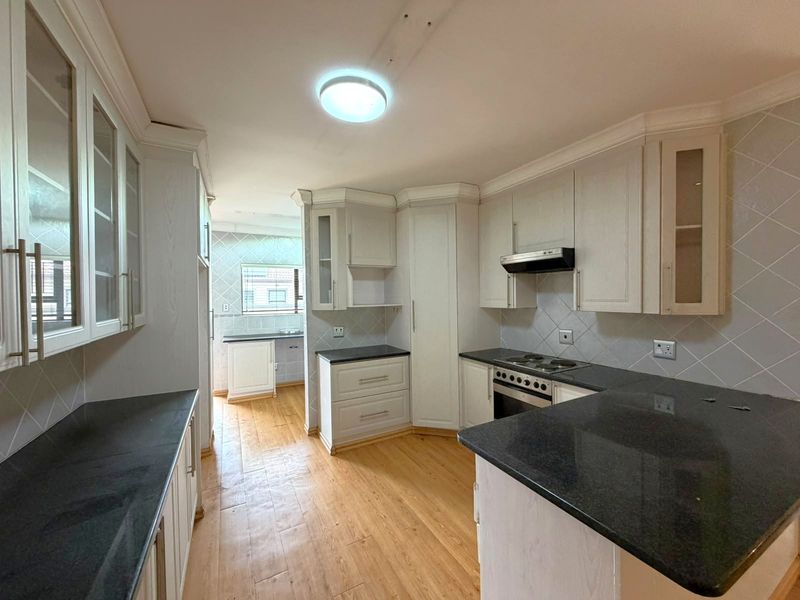 A spacious kitchen featuring light-toned built-in cabinetry, dark granite countertops, an electric hob, and an integrated oven with a tiled backsplash.