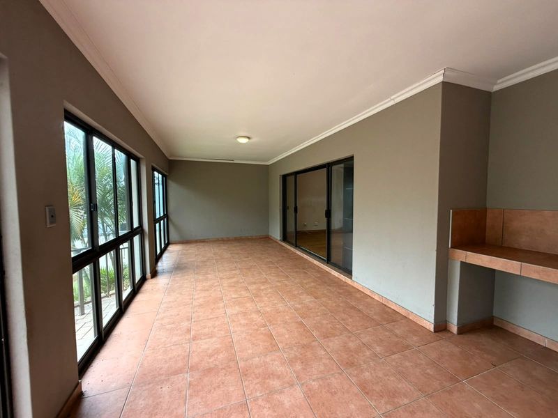 A spacious, empty covered patio featuring tiled flooring, large sliding glass doors, and a built-in counter area, ideal for outdoor entertaining.