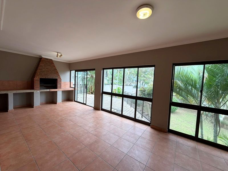 Spacious covered patio featuring a built-in brick braai, tiled flooring, and large aluminium sliding doors providing access to the garden.