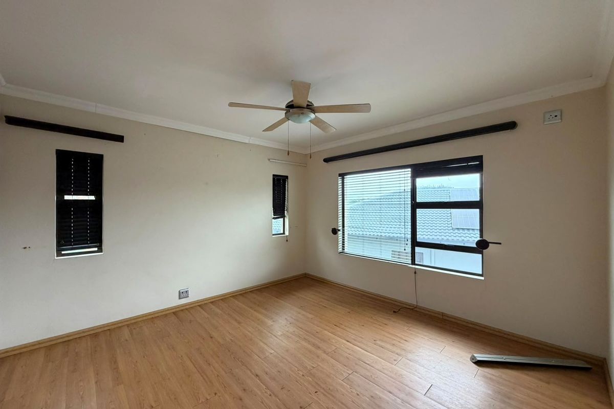 An empty bedroom featuring laminate flooring, a ceiling fan, and aluminium windows with fitted blinds, offering a neutral canvas for personalization.