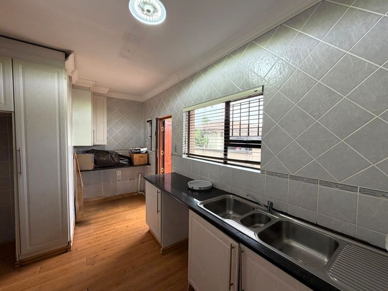 A functional kitchen featuring laminate cabinetry, dark stone countertops, a double bowl stainless steel sink, and diamond-patterned wall tiles.