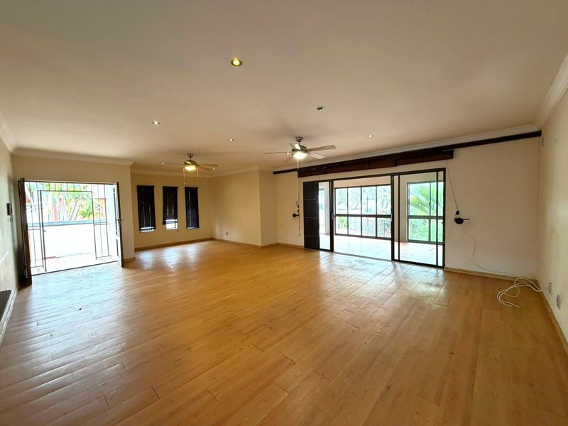 Spacious, open-plan living area featuring timber-look floor tiles, recessed downlights, ceiling fans, and large sliding glass doors providing access to the outdoor space.