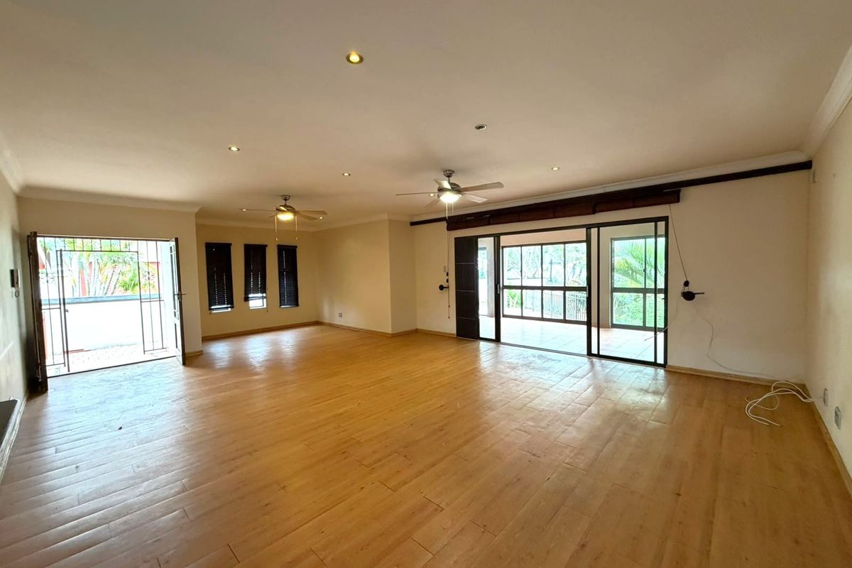 Spacious, open-plan living area featuring timber-look floor tiles, recessed downlights, ceiling fans, and large sliding glass doors providing access to the outdoor space.