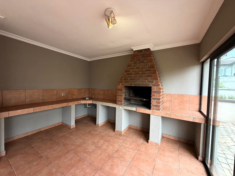 Covered patio area featuring a built-in brick braai, tiled workspace with integrated sink, and sliding glass doors leading to the exterior.