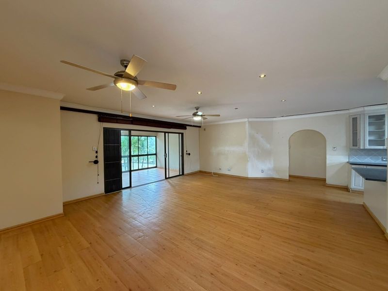 Spacious open-plan living area featuring laminate flooring, ceiling fans, and sliding doors leading to an outdoor patio, with an adjacent kitchen area.