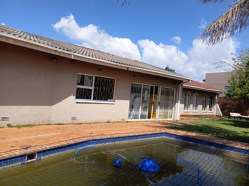 Rear exterior view of the house featuring a swimming pool, paved patio area, and security gates on the sliding doors and windows.