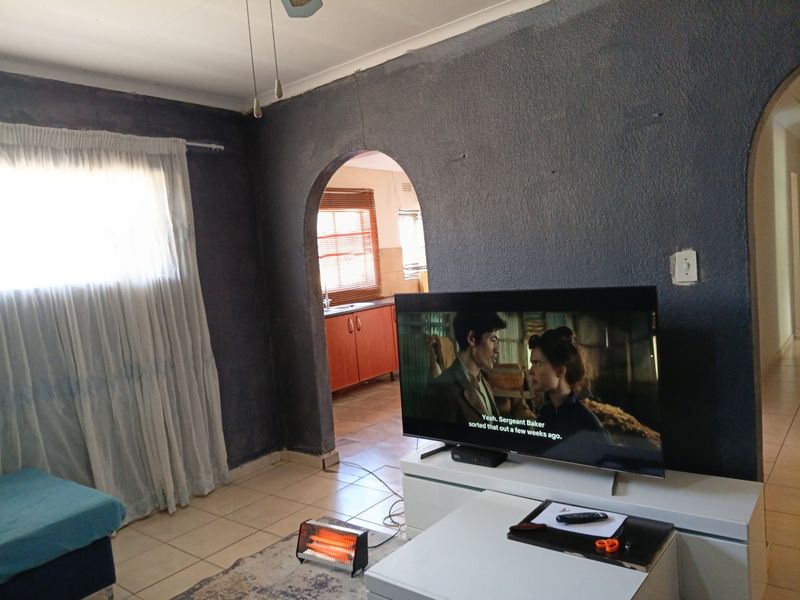 A living room featuring tiled floors, a distinctive arched doorway leading to the kitchen, and textured dark-painted walls with visible structural cracking.