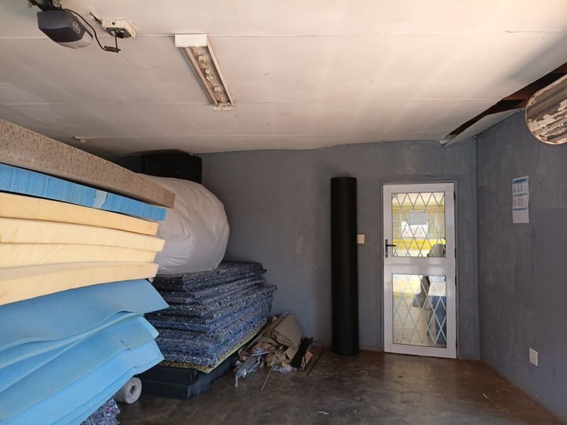 A functional garage space featuring a concrete floor, security door, and overhead lighting, currently used for storage.