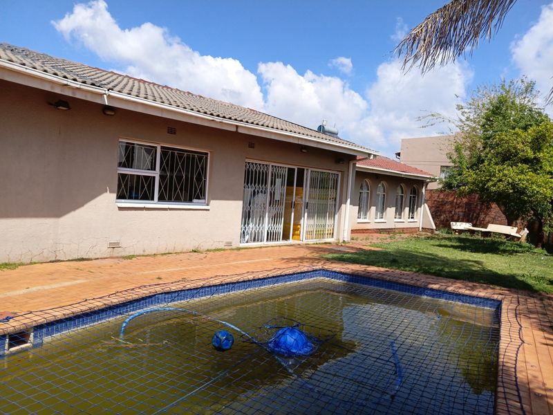 Rear exterior view featuring a swimming pool with safety net, paved patio area, and access to the house via sliding security doors.