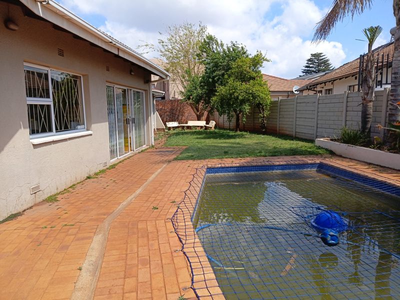 Rear garden area featuring a swimming pool with safety net, brick paved patio, and perimeter precast concrete walling.