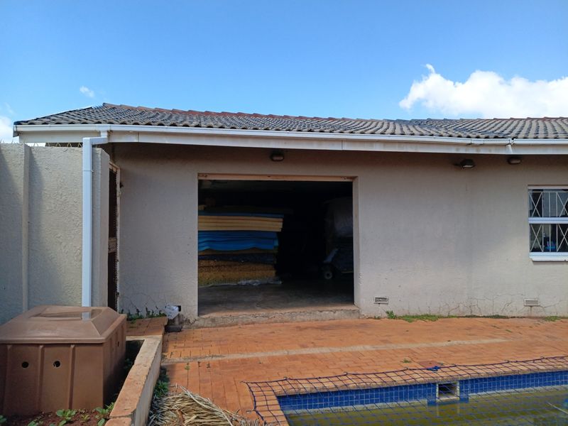 Rear exterior view showing a swimming pool, paved patio area, and access to a garage or storage space with visible wall cracking.
