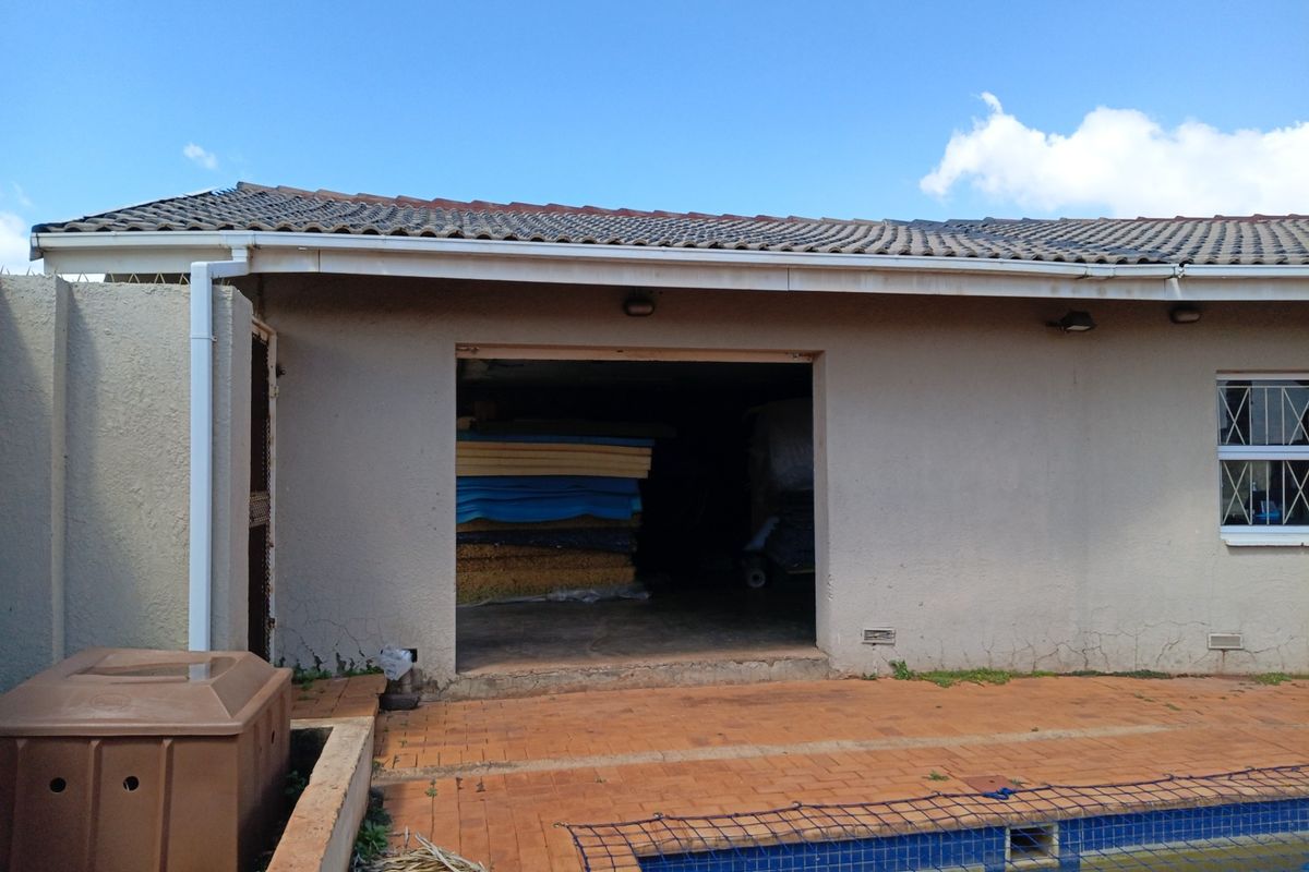 Rear exterior view showing a swimming pool, paved patio area, and access to a garage or storage space with visible wall cracking.