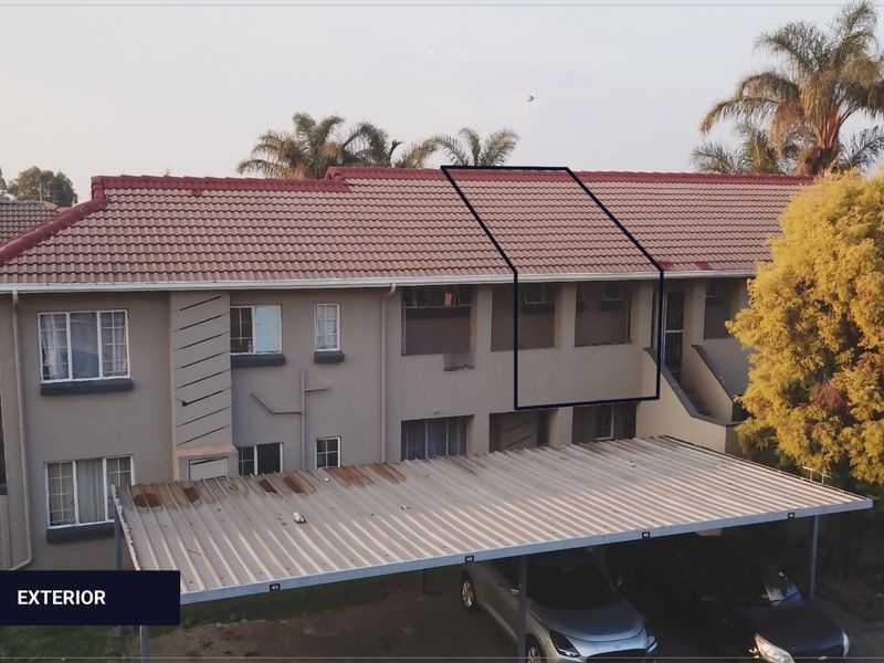 Front elevation of an apartment complex featuring a tiled roof, exterior facade, and a covered carport parking area.