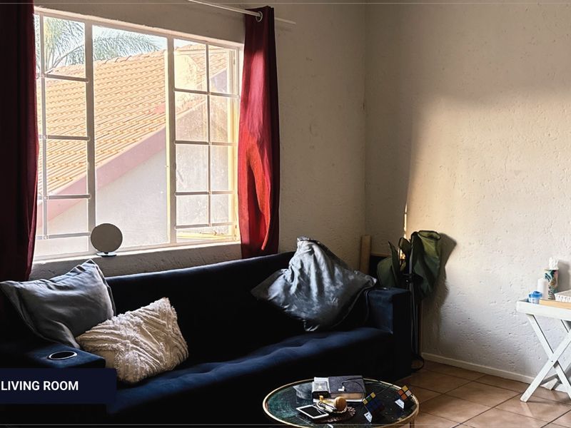 A living room area featuring tiled flooring and a window with security bars, providing natural light to the space.