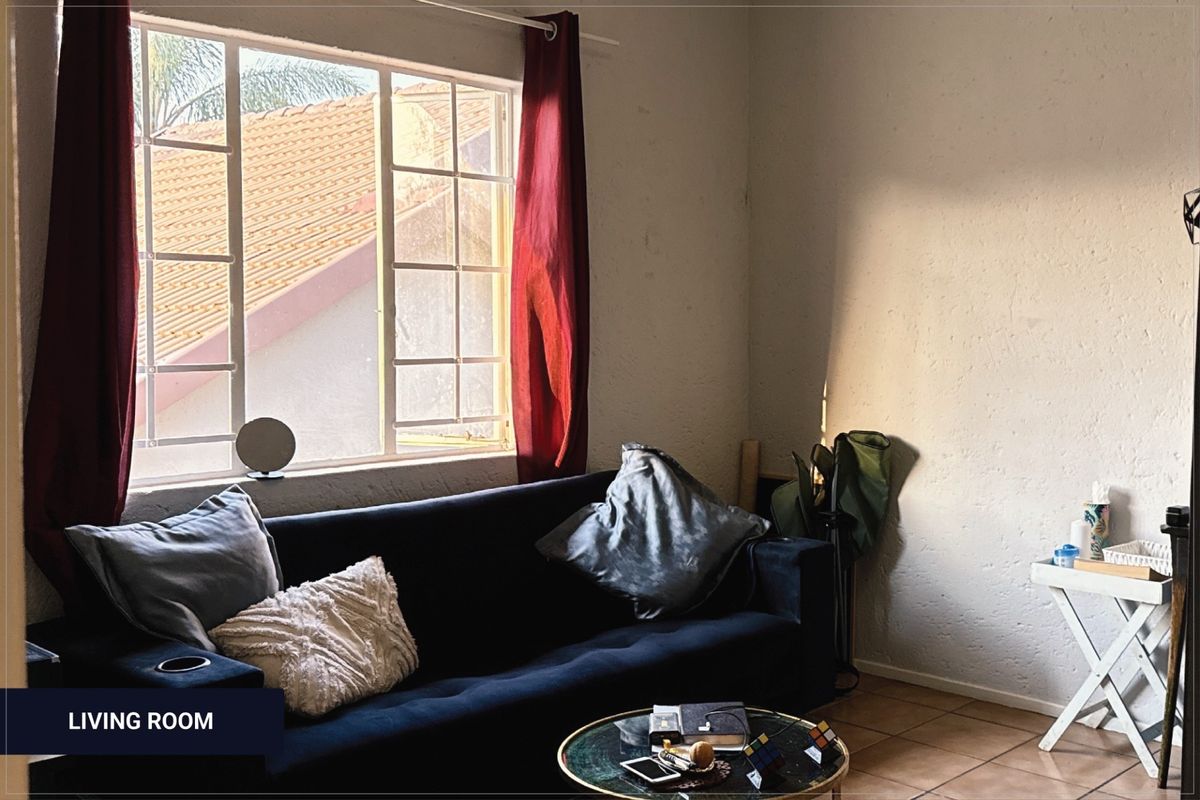 A living room area featuring tiled flooring and a window with security bars, providing natural light to the space.