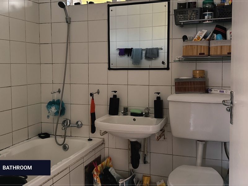 A compact bathroom featuring a bathtub with handheld shower, wall-mounted basin, and toilet, finished with white wall tiles.