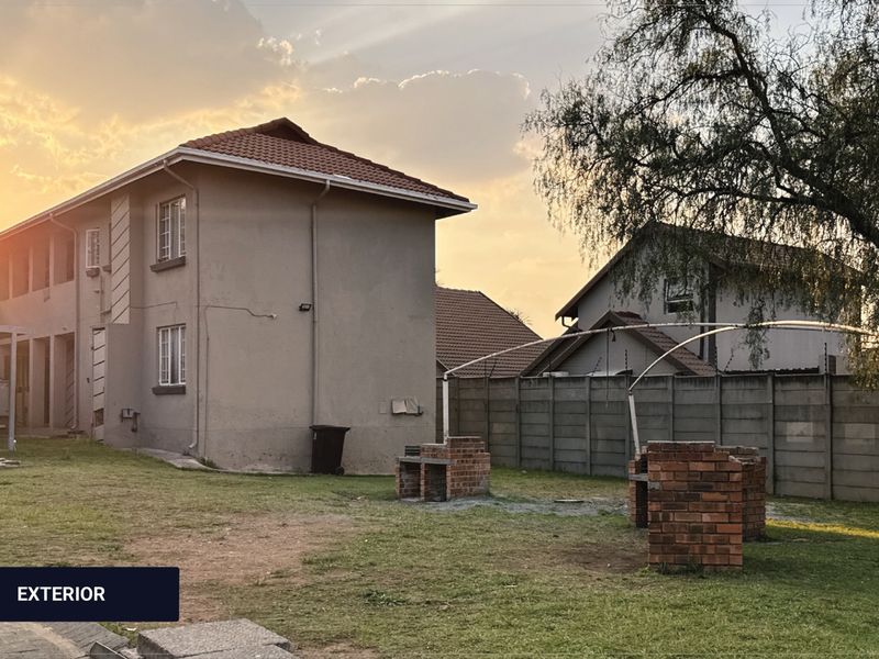 Rear exterior view of the apartment building featuring a communal garden area with brick braai facilities and perimeter walling.