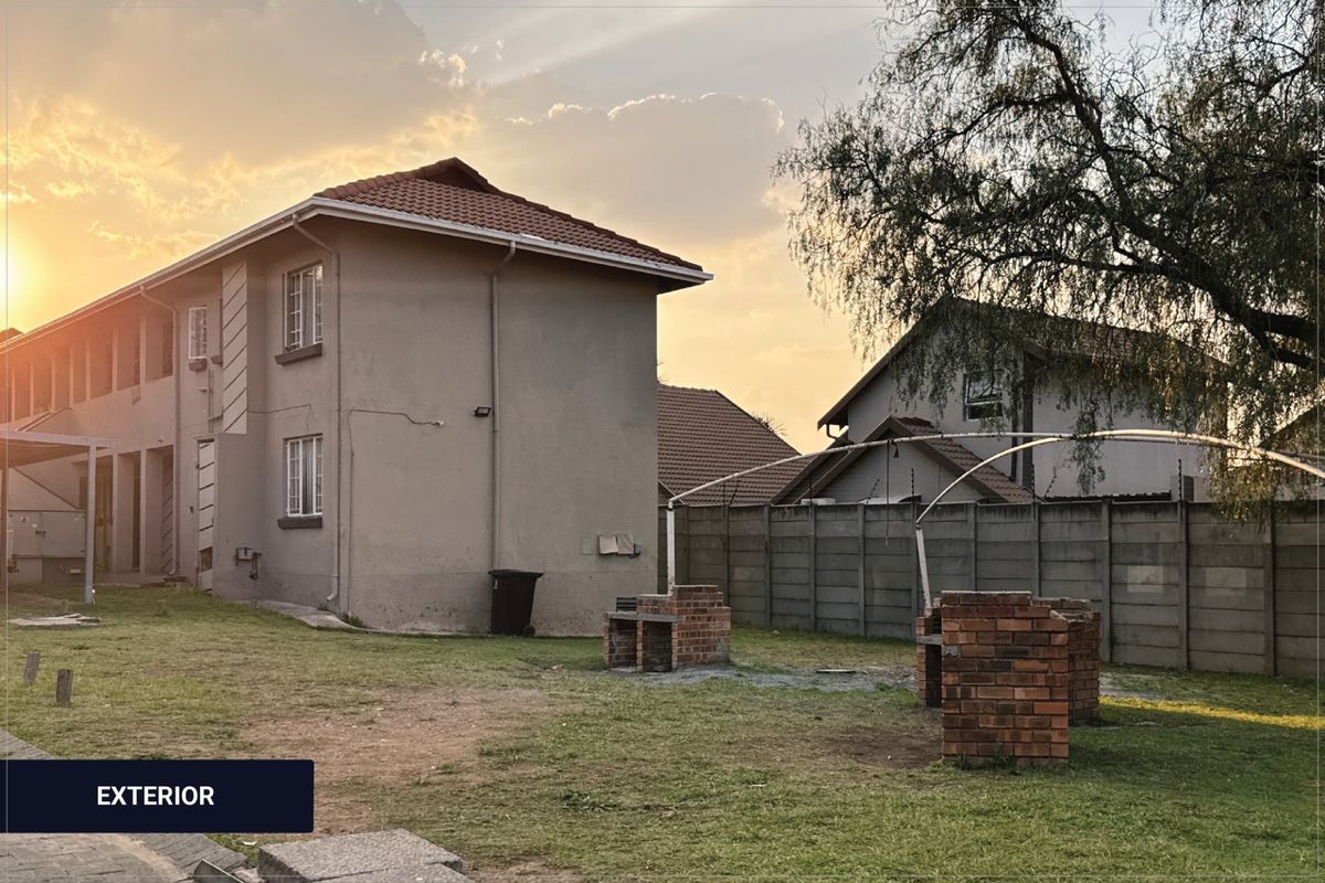Rear exterior view of the apartment building featuring a communal garden area with brick braai facilities and perimeter walling.