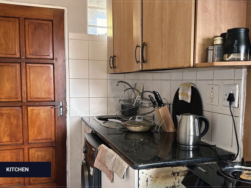 A compact kitchen featuring granite countertops, tiled backsplash, and timber cabinetry, showing signs of wear on the lower cabinet panels.