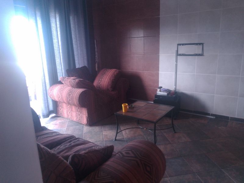 A living room area featuring tiled flooring and a tiled feature wall with a mounted television bracket, illuminated by natural light from a window.