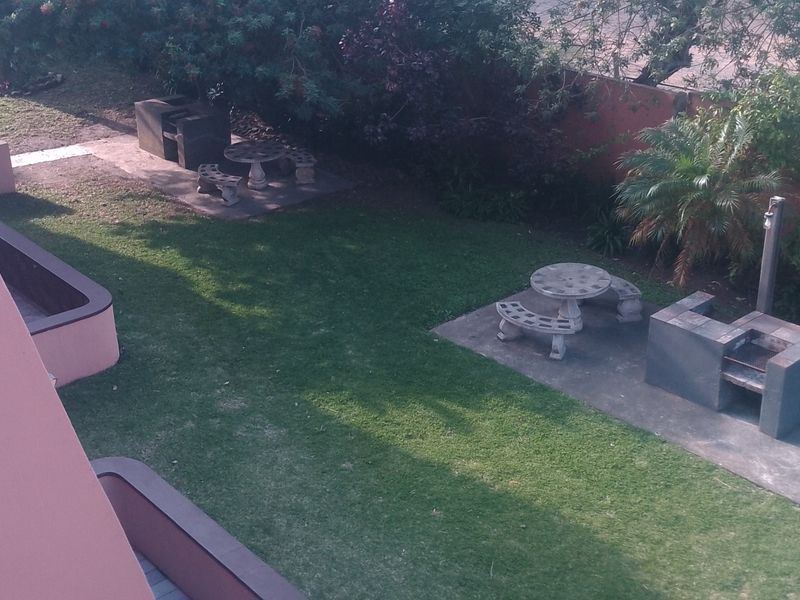 Communal garden area featuring built-in braai facilities and concrete seating areas set within a landscaped lawn space.