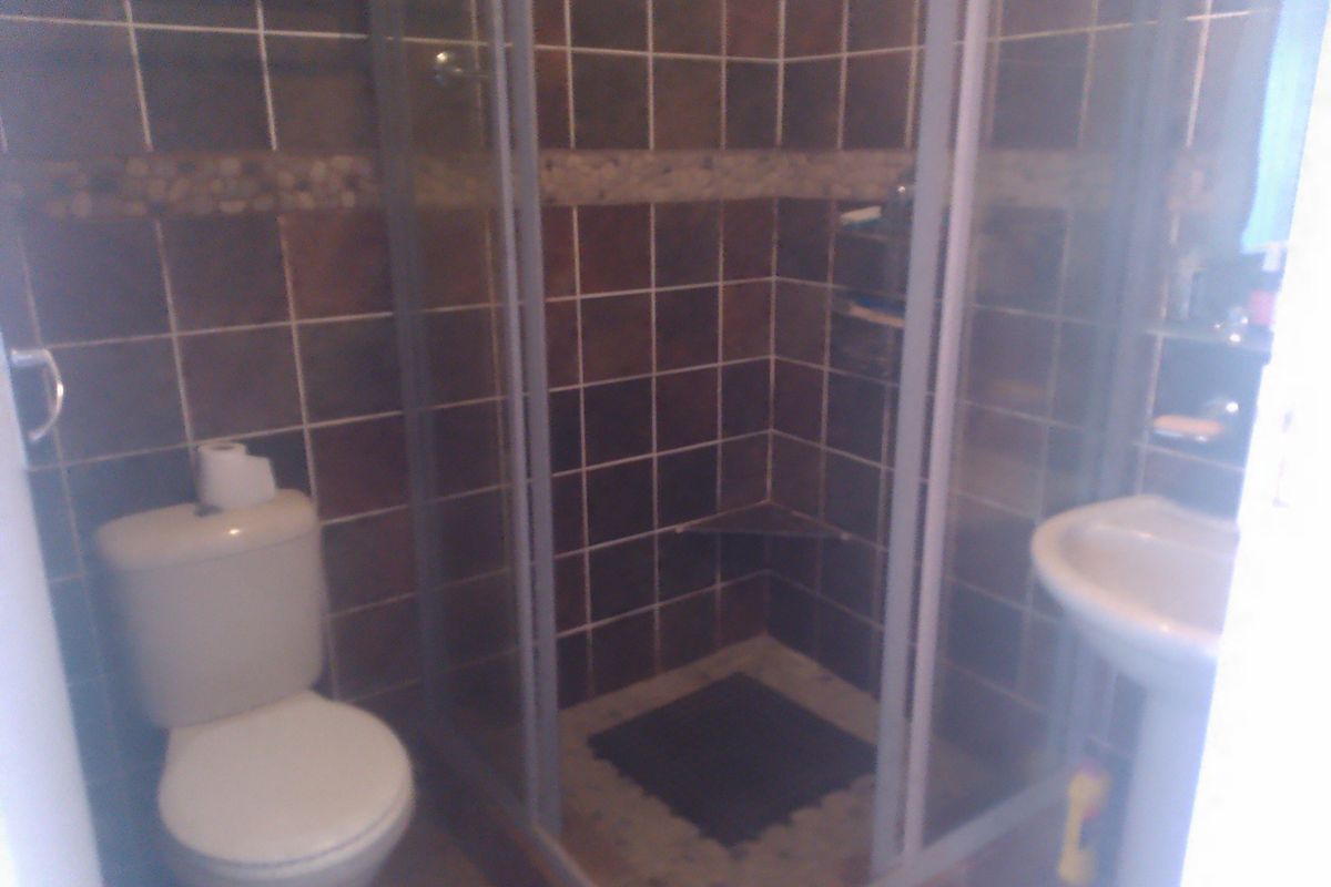 A compact bathroom featuring a shower enclosure, pedestal basin, and toilet with dark tiled wall finishes.