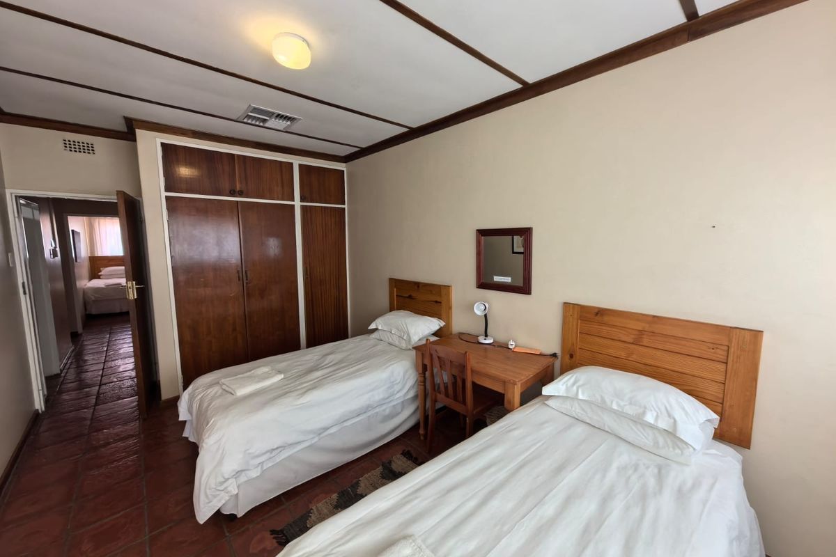 A bedroom featuring built-in wooden cupboards, terracotta floor tiles, and an exposed beam ceiling, offering a functional space with traditional finishes.