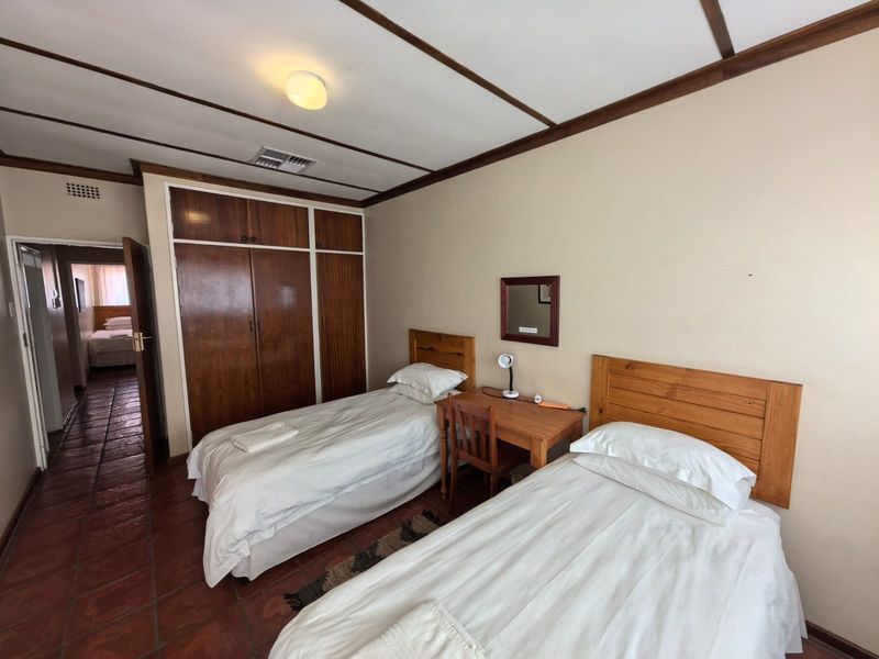A bedroom featuring built-in wooden cupboards, terracotta floor tiles, and an exposed beam ceiling, offering a functional space with traditional finishes.