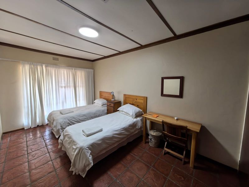 A bedroom featuring terracotta tile flooring, exposed beam ceiling, and a sliding glass door with curtains, providing a functional and well-lit space.