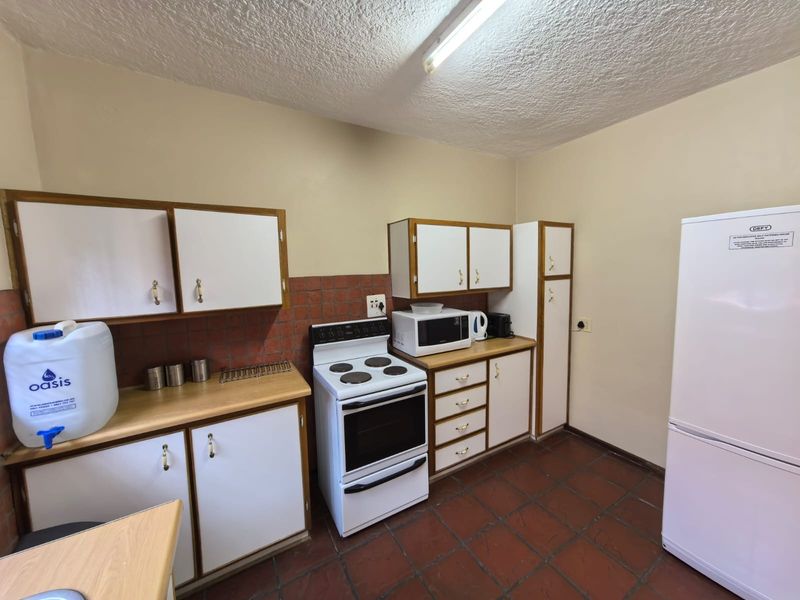 A functional kitchen featuring white cabinetry, laminate countertops, a tiled backsplash, and terracotta-style floor tiles, offering potential for modern updates.