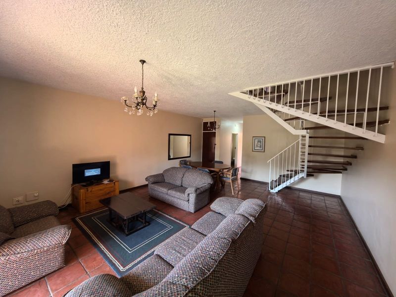 Open-plan living and dining area featuring terracotta floor tiles and a prominent staircase with white metal railings.