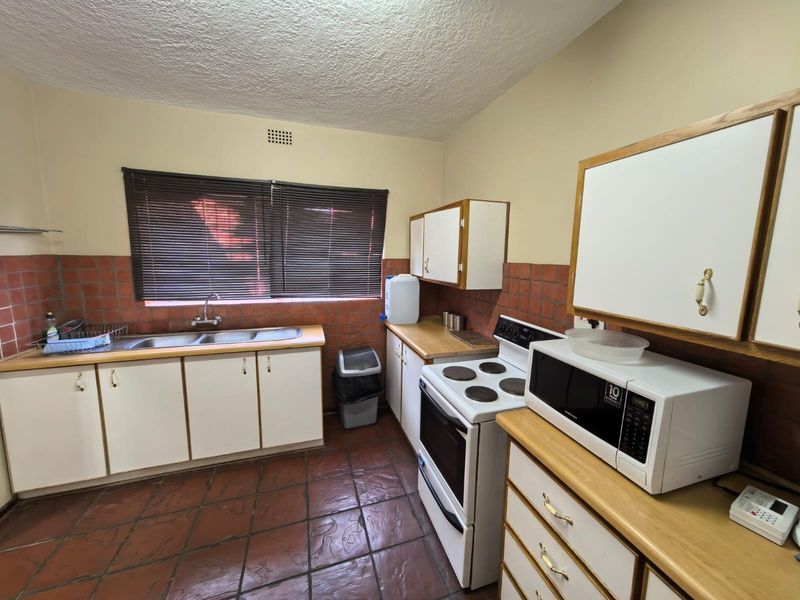 A functional kitchen featuring tiled flooring, a double basin sink, laminate countertops, and built-in cabinetry with a tiled splashback.