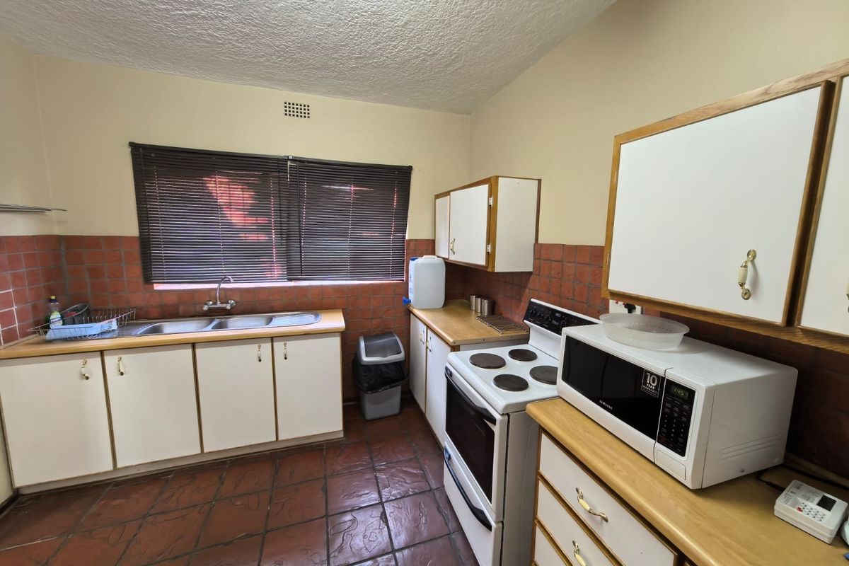 A functional kitchen featuring tiled flooring, a double basin sink, laminate countertops, and built-in cabinetry with a tiled splashback.
