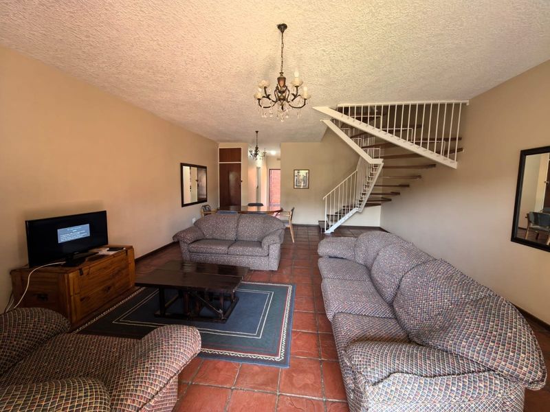 Spacious open-plan living area featuring terracotta floor tiles, a central staircase with metal balustrades, and a textured ceiling.