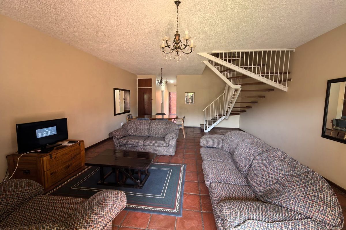 Spacious open-plan living area featuring terracotta floor tiles, a central staircase with metal balustrades, and a textured ceiling.