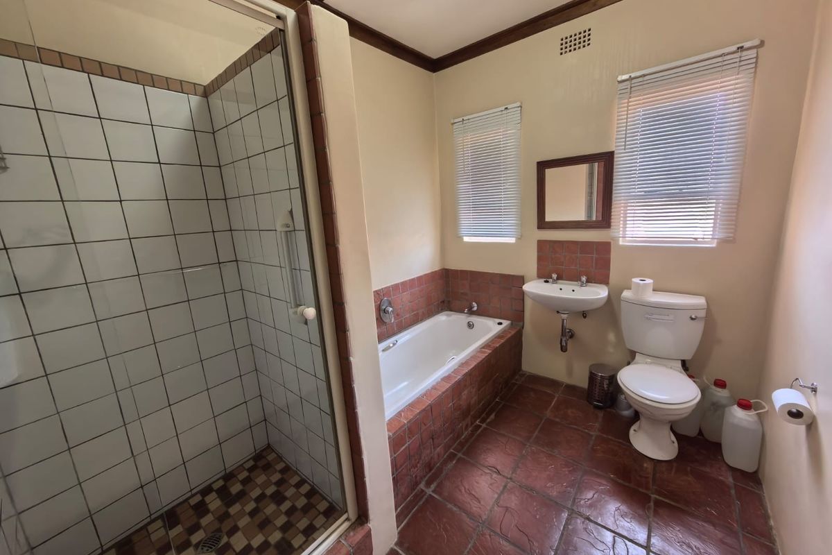 A functional bathroom featuring a separate shower enclosure, built-in bathtub, wall-mounted basin, and toilet with dated terracotta-style floor and wall tiling.
