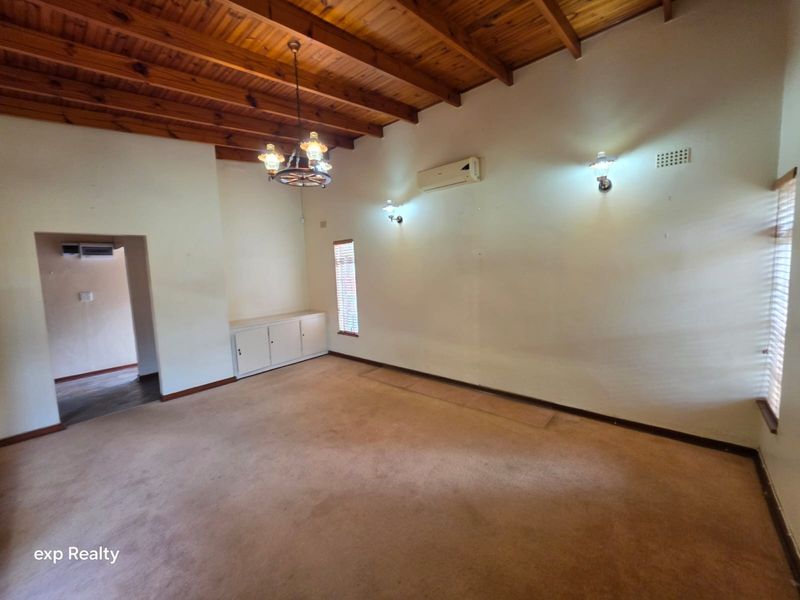 Spacious living room featuring an exposed timber beam ceiling, built-in cabinetry, wall-mounted air conditioning, and neutral wall finishes.