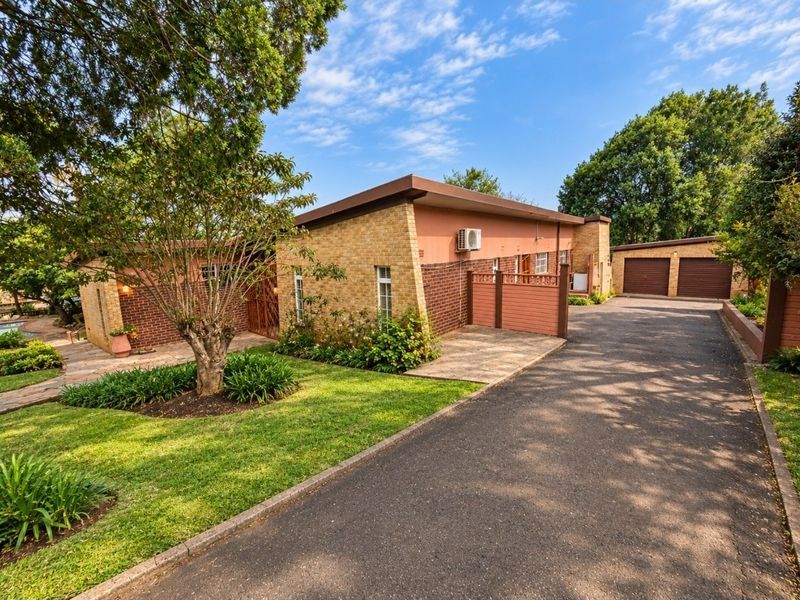 Front view of a brick house featuring a spacious asphalt driveway, double garage, and well-maintained landscaped garden area.