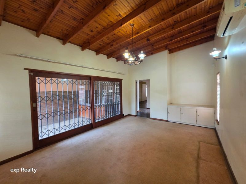 Spacious living room featuring an exposed timber beam ceiling, built-in cabinetry, and large sliding doors with security gates leading to the exterior.
