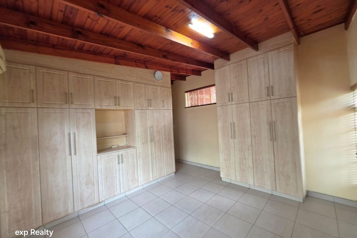 A spacious bedroom featuring extensive built-in cabinetry, tiled flooring, and a rustic exposed timber beam ceiling.