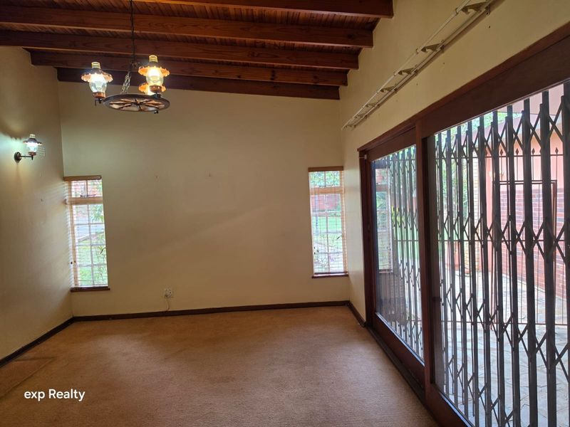 Spacious living area featuring exposed timber beam ceilings, carpeted flooring, and large sliding glass doors with security gates leading to the exterior.