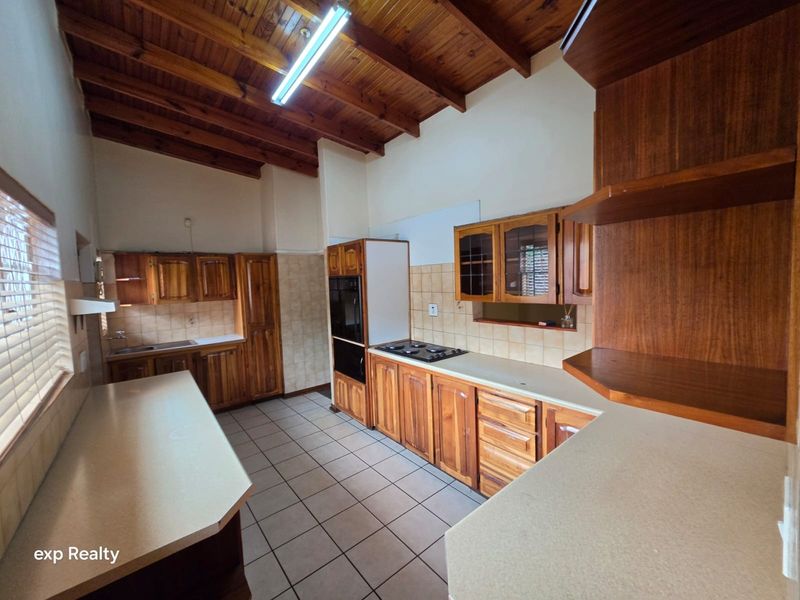 Spacious kitchen featuring extensive wooden cabinetry, built-in oven and hob, tiled flooring, and a high exposed timber beam ceiling.