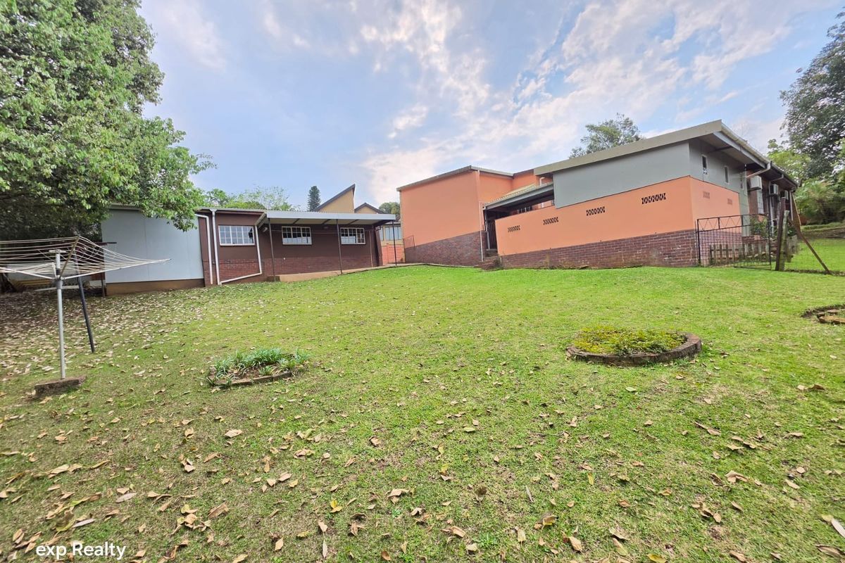 A view of the rear exterior of the house featuring a large lawn area and brick and painted wall finishes.